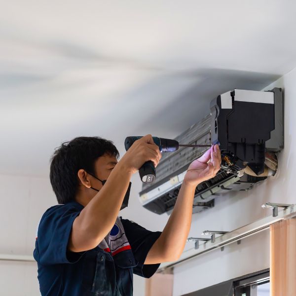 A precision air employee holding a drill while repairing a ductless mini-split in a customers home.